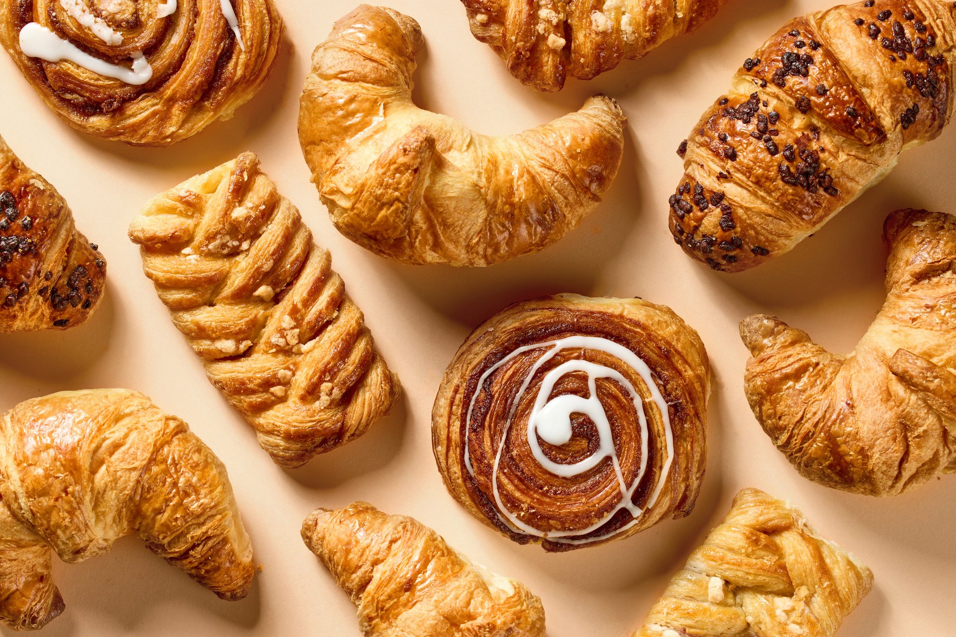 Assorted fresh bakery pastries and croissants arranged on a warm neutral background